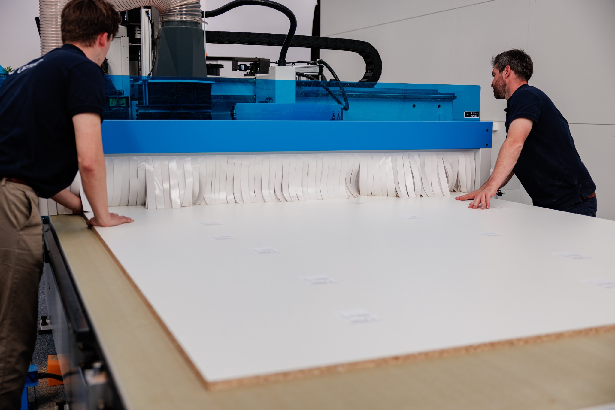 Twee medewerkers positioneren een plaat op een CNC-machine met een blauwe veiligheidskap.