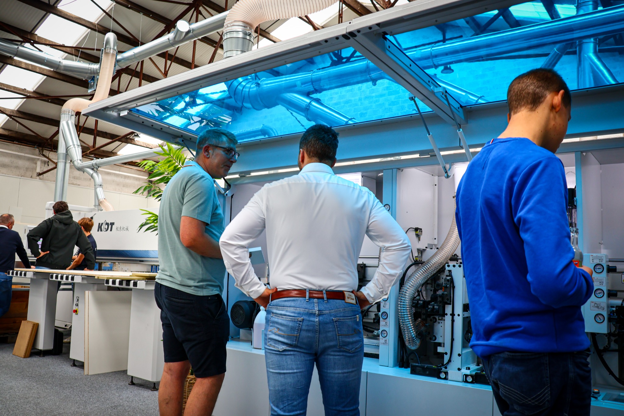 Bezoekers bekijken een KDT-machine met geopende blauwe kap tijdens een demonstratie.