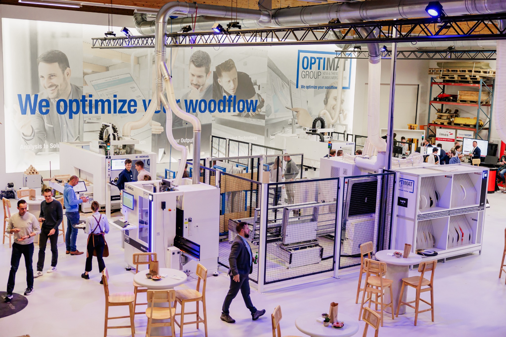 Overzicht van de OPTIMAT-showroom met houtbewerkingsmachines en bezoekers.